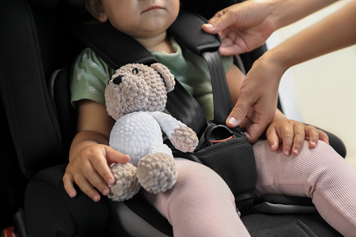 Mother fastening her daughter in child safety seat inside car, closeup