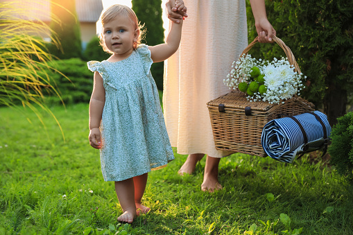 Adorable baby girl and her mother with picnic basket in garden on sunny day