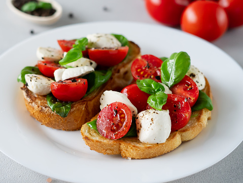 Toast with mozzarella cheese, tomatoes and basil leaves on light background. Italian food. Close-up