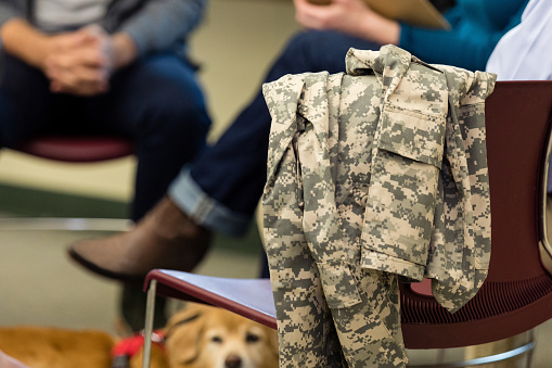 Unrecognizable veterans and an emotional support animal are in the background of the photo with a BDU jacket in focus in the foreground.
