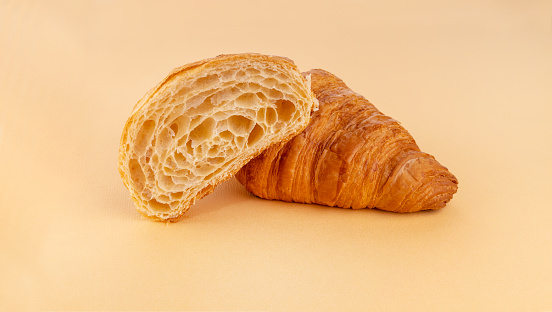 One plain croissant and half cut croissant on beige background
