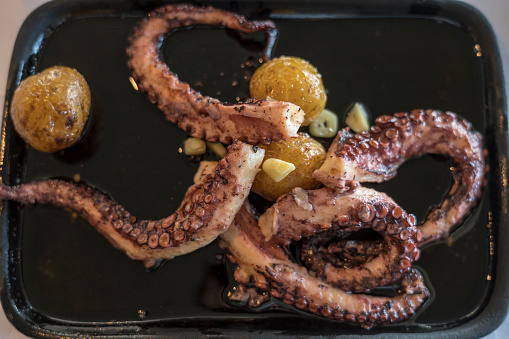 Portion of delicious grilled octopus with baked potatoes on black plate. Azores.