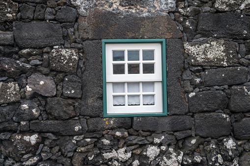 Small picturesque village, houses made of volcanic rocks, white window on the wall made of volcanic rocks. Cabrito, Pico island, Azores