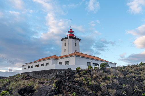 Lighthouse at the tip of Pico island, on volcanic landscape against blue sky, Azores archipelago