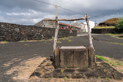 Old water well in picturesque village, houses made of volcanic rocks, at the edge of black lava coast. Cabrito, Pico island, Azores