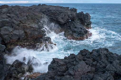 High waves at black volcanic coast, Pico island, against blue sky, Azores archipelago