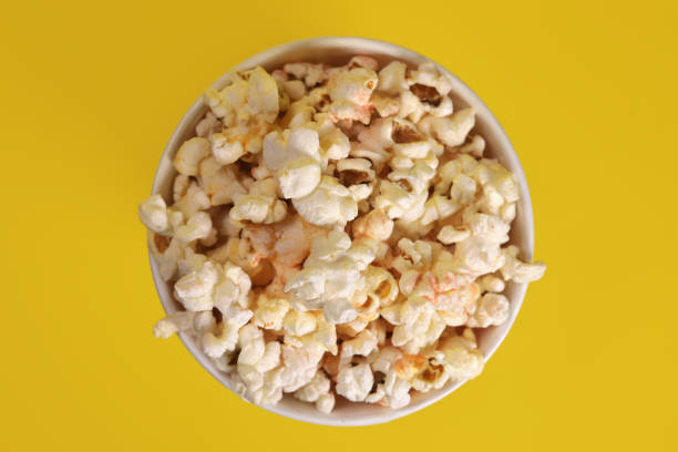 istock Paper cup with popcorn on yellow background, top view 1487117389