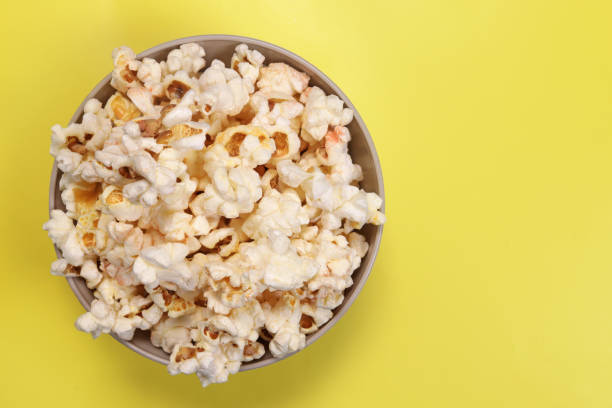 istock Paper cup with popcorn on yellow background, top view 1487117542
