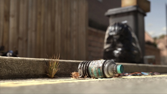 A discarded water bottle lies close to the kerb, with a bin in the background and a black garbage bag.