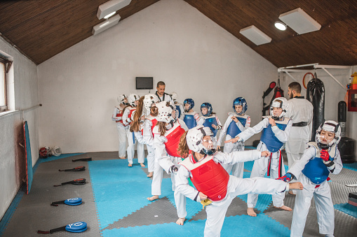 A group of children, dressed in kimonos, practice taekwondo together, led by a martial arts coach