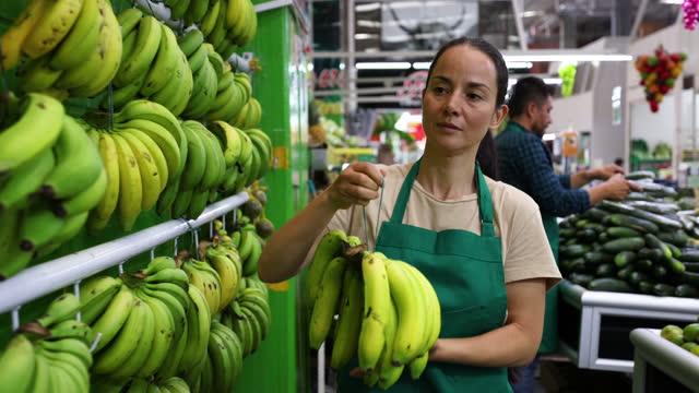 Woman organizing the banana display at a greengrocer’s market