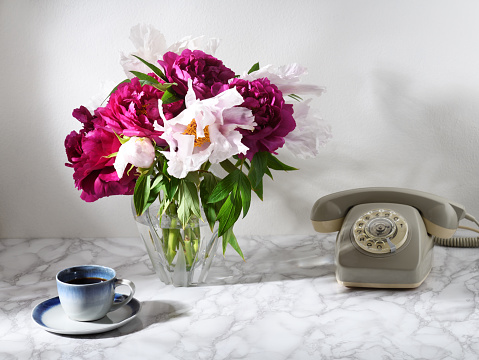Restro styled still life with telephone, cup of coffee and peonies