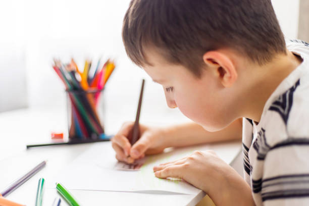 istock A child boy draws on white paper with colored pencils while sitting at a table 1487126714