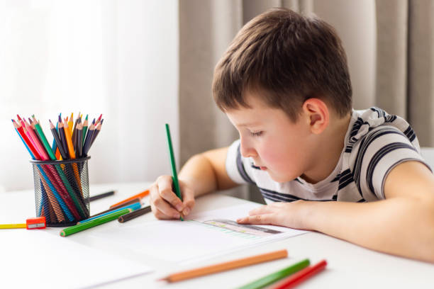 istock A child boy draws on white paper with colored pencils while sitting at a table 1487126731