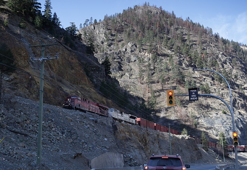 Fraser Canyon, Canada - April 2, 2023: Traffic on the Trans-Canada Highway waits at the railroad crossing as CPR 8794 heads north near the Thompson River through southern British Columbia. Spring morning in the Thompson-Nicola Regional District.