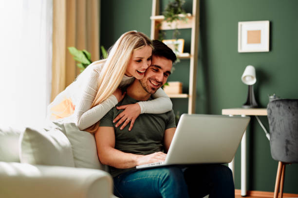 Hermosa pareja joven y feliz que tiene videollamada a través de una computadora portátil en casa - foto de stock