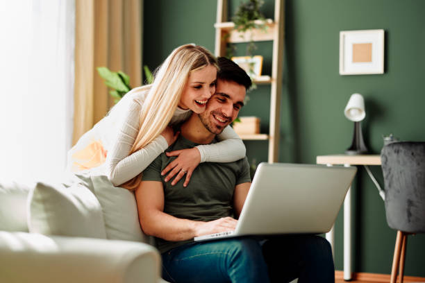 自宅でノートパソコンでビデオ通話をする美しい若い幸せな夫婦 ストックフォト