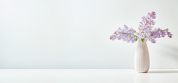 Lilac branches in a vase on a white table with copy space