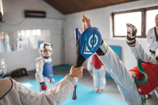 Two young female judokas training in the gym, one is grabbing her opponent and throwing her on the floor