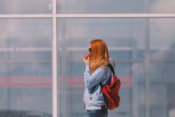 Woman is walking in the city and eats ripe apple fruit