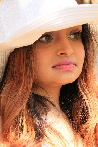 A closeup of a Fijian model wearing a white hat. She has long brown hair, and makeup.