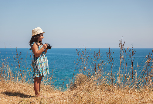 Happy little girl on vacation photographing by the sea with her vintage camera