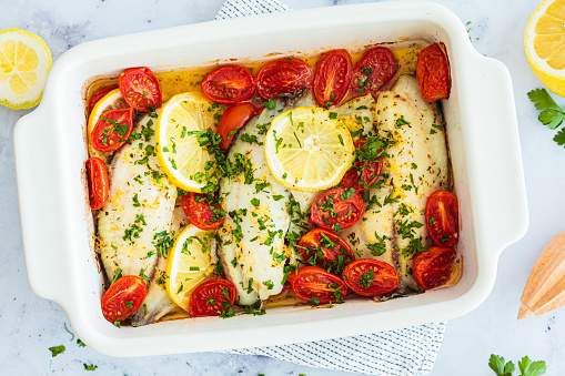 Baked cod fillet with cherry tomatoes and butter, top view. Healthy diet recipe.
