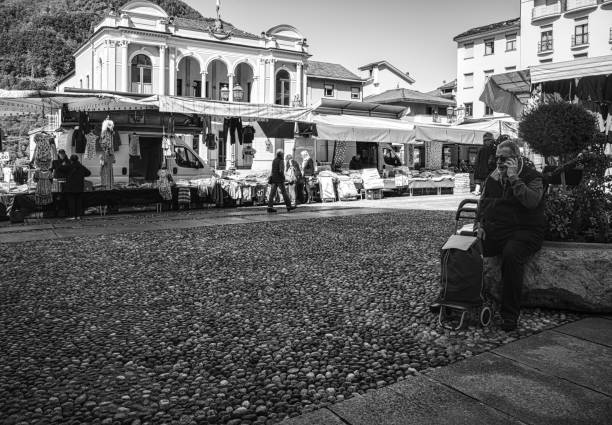 Varallo Sesia, Italy - May 02, 2023: People visita street market in the center of city. a man sitting in a bench