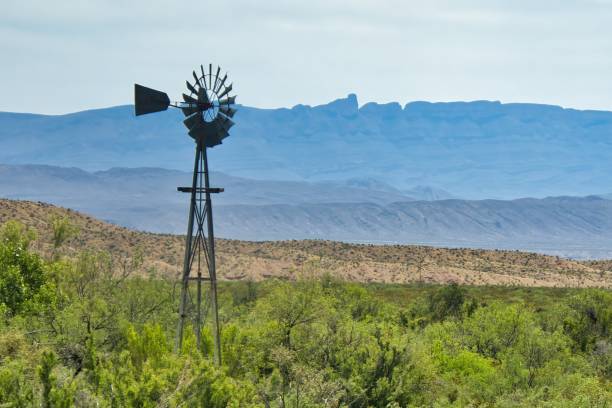 On a day in late April, hazy mountains provide the backdrop for an abandoned windmill surrounded by green desert shrubs at Big Bend National Park in Brewster County, TX.