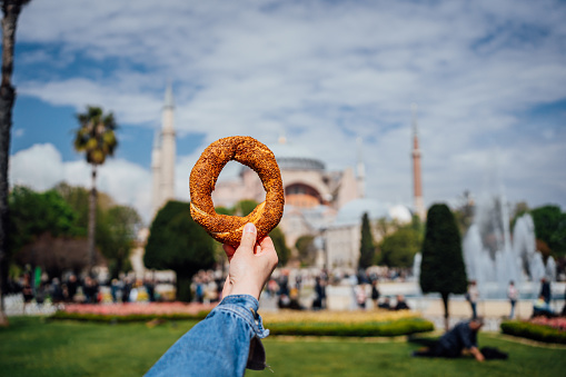 Woman's hand holding a bagel-simit in front of Hagia Sophia in Istanbul, Turkey