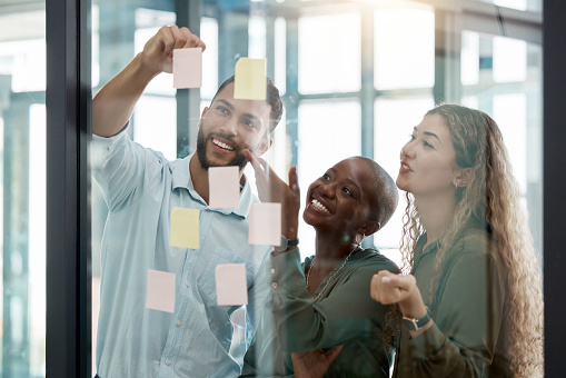 Diversity, collaboration and team in a business brainstorming strategy for planning and sticky notes. Creative people sharing ideas, plan and schedule work tasks in teamwork and delegation at office.