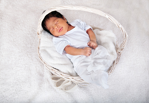 Sweet sleeping African-American newborn baby boy swaddled in a blanket and lying in a basket