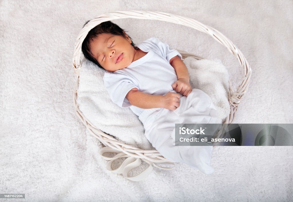 Sweet sleeping African-American newborn baby boy swaddled in a blanket and lying in a basket 0-1 Months Stock Photo