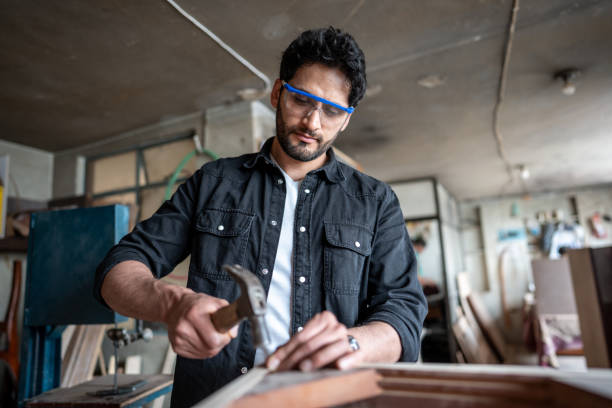 Mid adult carpenter hammering a nail on piece of wood at carpentry Mid adult carpenter hammering a nail on piece of wood at carpentry work tool nail wood construction stock pictures, royalty-free photos & images