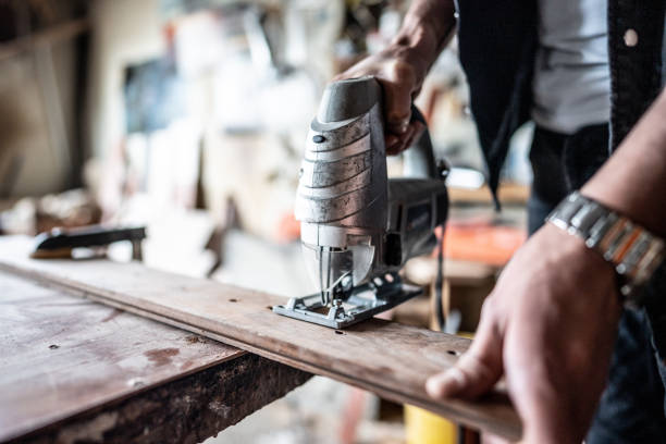 Close-up of a nan using an electric jigsaw at carpentry workshop