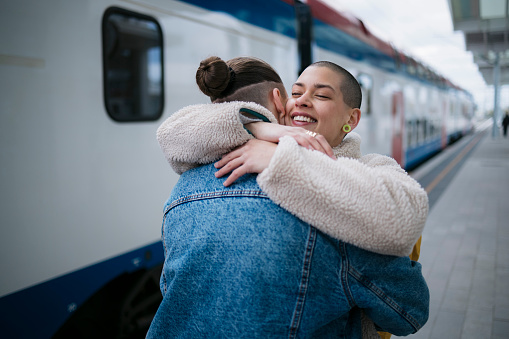 Woman leaving and embracing her friend on train station. Female greeting good by with a hug to a friend on railway station platform.