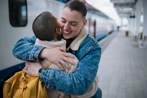 Cheerful young female embracing her friend on railway station platform. Female couple hugging each other on train station.
