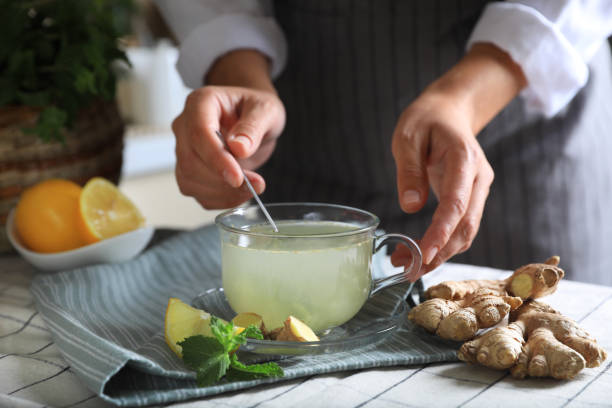 Woman making aromatic ginger tea at table indoors, closeup