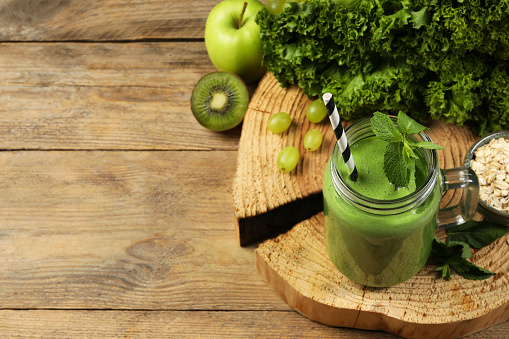 Mason jar of fresh green smoothie and ingredients on wooden table, space for text