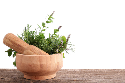 Mortar, pestle and different herbs on wooden table against white background. Space for text
