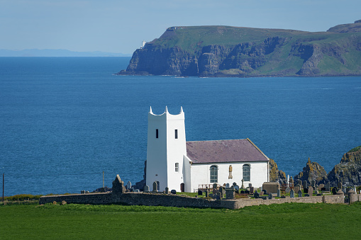 White colored parish church at Ballintoy, on the north coast of County Antrim, Northern Ireland, on a bright sunny day with the cliffs of Rathlin Island in the distance