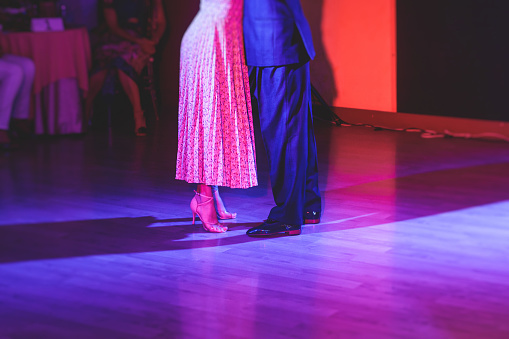 Couples dancing traditional latin argentinian dance milonga in the ballroom, tango salsa bachata kizomba lesson in red and purple lights, dance school class festival