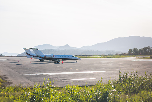 View of modern private reactive aircraft on an runway airfield ready to take off, airstrip with business jet airplane before the flight with mountains in the background, summer sunny day