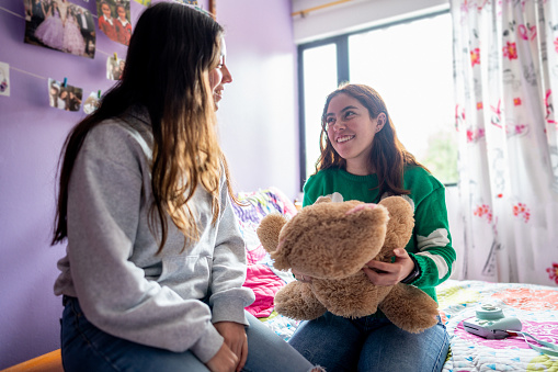 Young twin sisters remember good times with teddy bear on bedroom at home