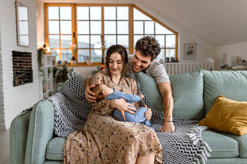 Smiling young parents with their baby boy sitting in sofa at home, cuddling.