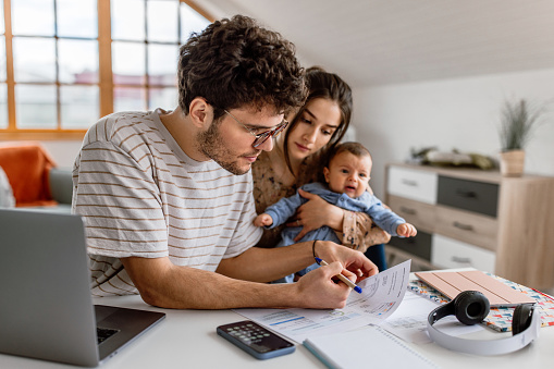 Young parents taking care for cute little baby while doing financial planning at home