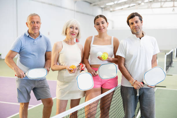 jugadores de pickleball sonrientes con raquetas y pelotas posando en la cancha - tennis court tennis net indoors fotografías e imágenes de stock