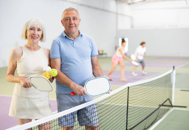 coppia anziana con racchette e palline in posa sul campo da pickleball - tennis men indoors serving foto e immagini stock