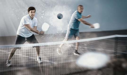 Focused resolved adult man playing friendly pickleball match in team with older partner on closed court. Concept of concentration in competition