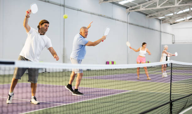 uomo adulto che gioca doppio pickleball con partner anziano al chiuso - tennis men indoors serving foto e immagini stock